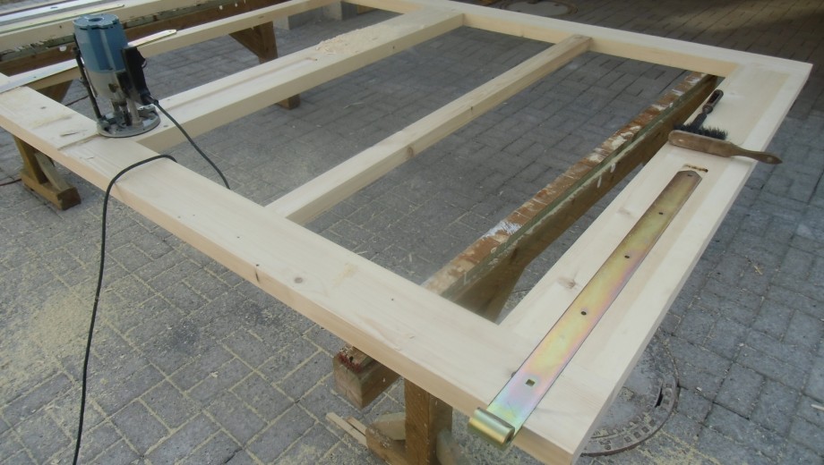 Eine Werkbank im Freien mit Holzrahmen, Oberfräse, Schraubenzieher und Metallbeschlag für Holzbearbeitung.