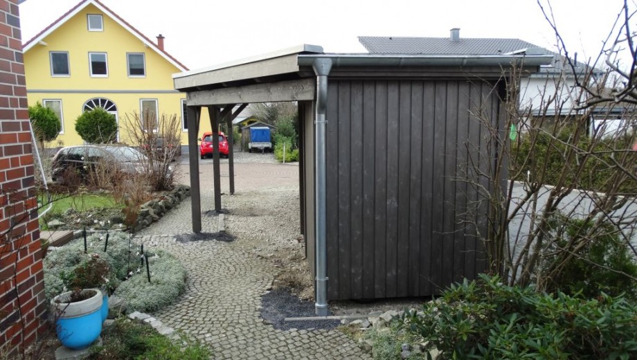 Ein ruhiges Wohngebiet mit einem Carport, einem gelben Haus im Hintergrund und grünen Pflanzen.