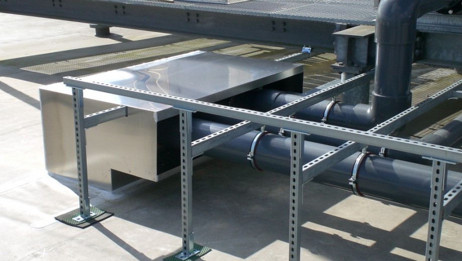 Industrielle Installation mit großen Rohren und glänzendem Metallgehäuse auf grauem Untergrund.