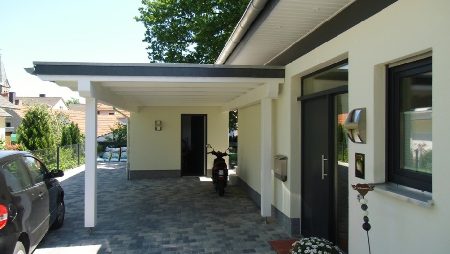 Moderner Carport neben einem Haus mit geparktem Auto und Motorrad, umgeben von gepflegter Umgebung.