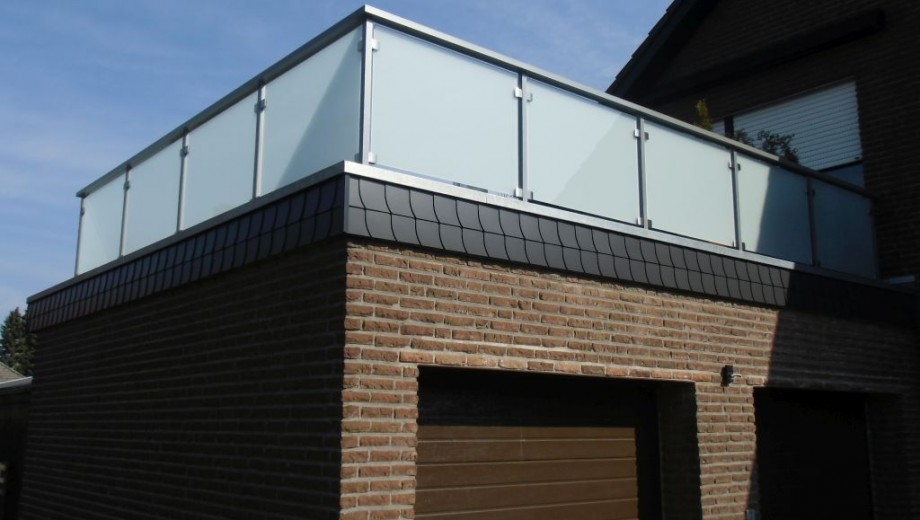 Modernes Gebäude mit Flachdach, Glasbalustrade und Ziegelwänden unter blauem Himmel.