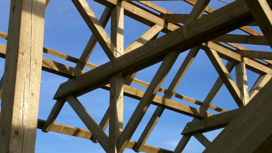 Holzdachkonstruktion vor blauem Himmel, Balken in Gittermuster, stabile und rustikale Bauweise.