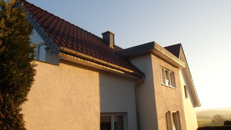 Modernes zweistöckiges Haus mit rotem Ziegeldach in ländlicher Umgebung bei warmem Sonnenlicht.