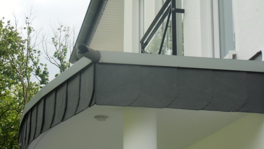 Moderner Balkon mit dunkler Verkleidung, Metallgeländer und grünem Hintergrund. Elegante, klare Linien.