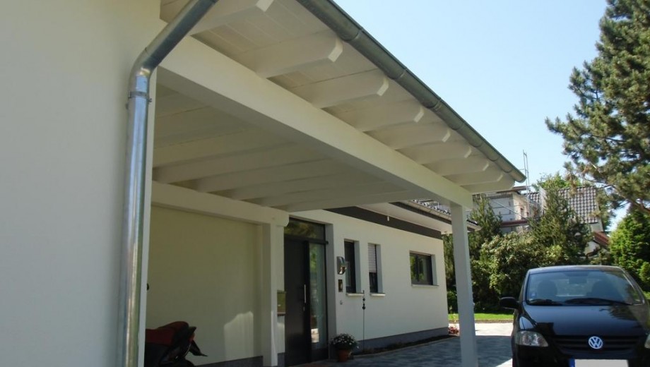 Moderner Hauseingang mit Carport, schwarzem Auto und weißer Fassade unter klarem, blauem Himmel.