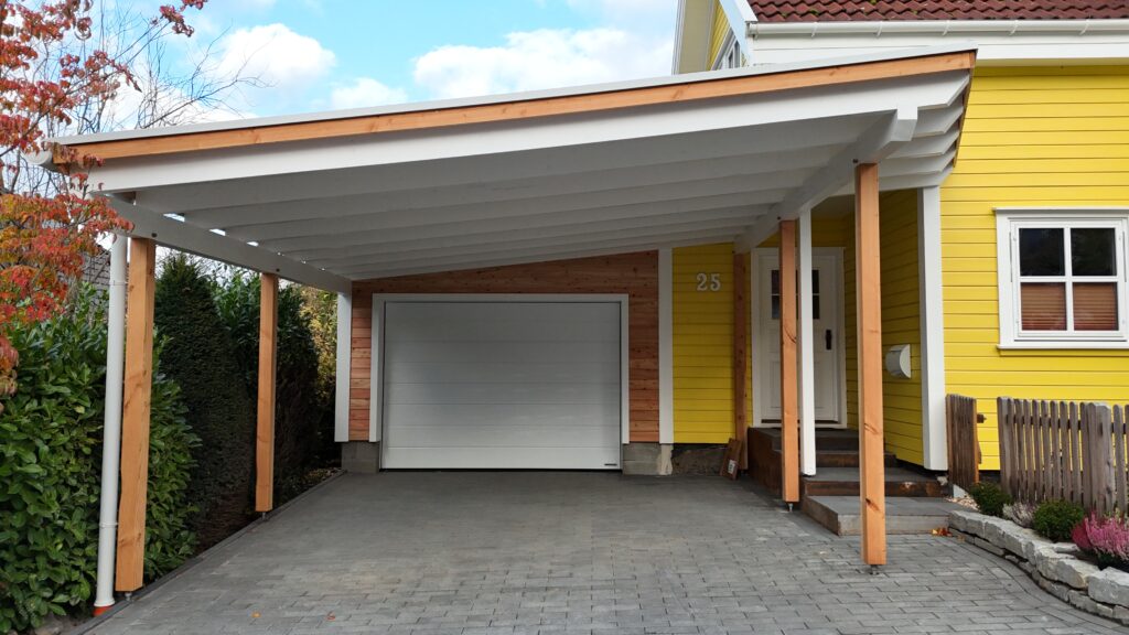 Moderne Einfahrt mit gelbem Haus, weißem Carport und Garage, umgeben von grünen Pflanzen.