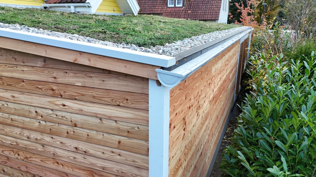 Ein Gebäude mit Holzverkleidung und begrüntem Dach, umgeben von Steinen und einer Regenrinne.