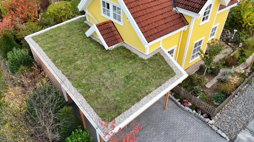 Ein gelbes Haus mit rotem Ziegeldach, begrüntem Flachdach und gepflegtem Garten in ruhiger Umgebung.