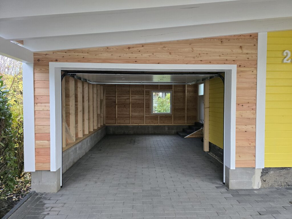 Eine leere, offene Garage mit Holzpaneelen und grauem Pflasterboden, umgeben von gelben Wänden.