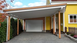 Moderne Einfahrt mit gelbem Haus, weißem Carport und Garage, umgeben von grünen Pflanzen.