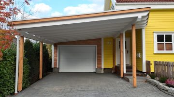 Moderne Einfahrt mit gelbem Haus, weißem Carport und Garage, umgeben von grünen Pflanzen.