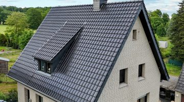 Einfamilienhaus mit steilem, dunkelgrauem Satteldach und heller Ziegelfassade in ruhiger Umgebung.