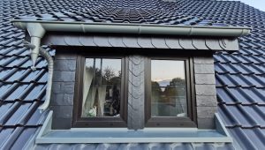 Ein Dach mit glänzenden dunkelblauen Ziegeln und einem zentralen Dachfenster mit dunklen Rahmen.