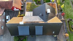 Luftaufnahme eines modernen Wohnhauses mit Solarpaneelen auf dem Dach, umgeben von Grünflächen.