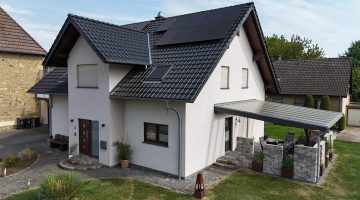 Modernes Einfamilienhaus mit Solarpaneelen auf dem Dach, umgeben von gepflegtem Garten.