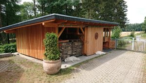 Ein Holzschuppen mit zwei ruhenden weißen Hunden davor, umgeben von Pflanzen in ländlicher Idylle.