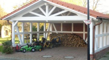 Überdachter Unterstand mit Holzstapeln, Kinderspielzeug und Fahrrädern; ländliche, familiäre Umgebung.