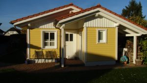 Ein gelbes Haus mit rotem Ziegeldach, umgeben von Gartenstühlen und Topfpflanzen, strahlt Gemütlichkeit aus.