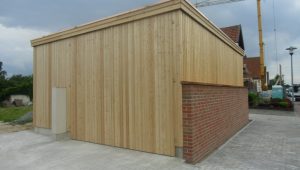 Ein rechteckiges Gebäude aus Holz und Ziegeln vor bewölktem Himmel, mit Kran im Hintergrund.